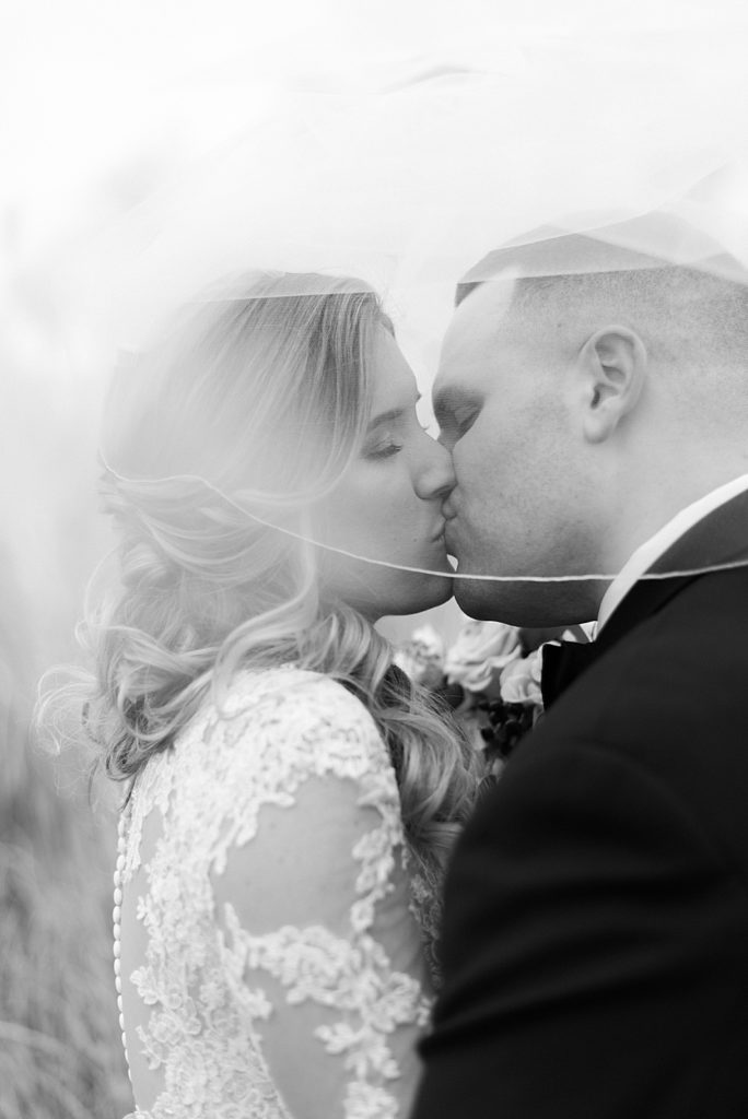 bride and groom kiss behind veil black and white